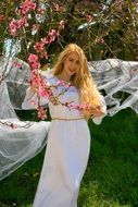 beauty of a girl with blond hair on the background of flowering tree branches in spring