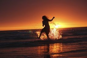 girl splashes on the beach at sunset