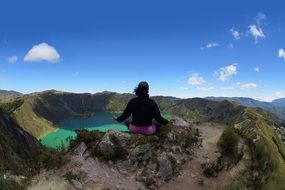 woman sitting on rock above green lake, ecuador, quilotoa