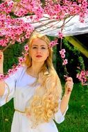 beauty of a girl with long blond hair on the background of flowering tree branches in spring
