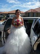 bride in wedding dress at car