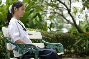 relaxed asian girl is sitting on a park bench