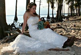 bride sits on beach back to sea