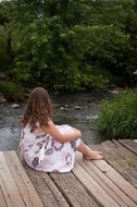 lonely girl is resting on a wooden pier on a river