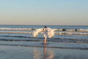 Woman in white angel wings on sea beach