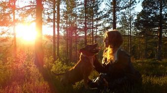 woman with dog in the forest at sunset