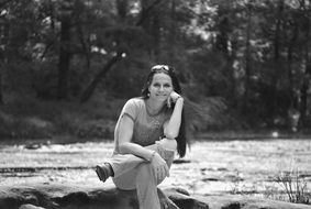 black white photo of a young woman on a stone by the river