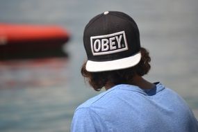 boy in black and white cap in front of water, back view