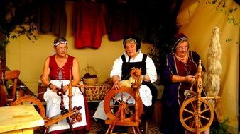 women sit near medieval spinning wheels