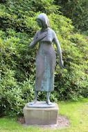 bronze statue of a woman near green bushes