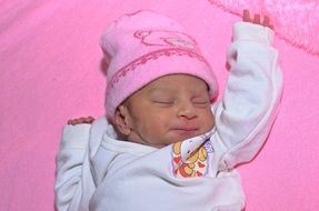 asian baby girl in pink hat sleeps on her back