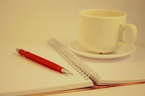 white cup on the background of a notebook with a pen