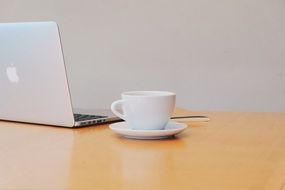 macbook and a white cup of coffee on a working desk