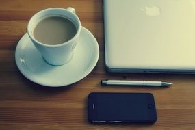 cup of coffe, a phone and a pen next to a macbook