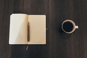 empty notebook with a pen and coffee on a desk