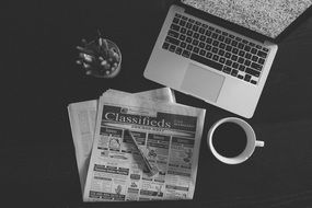 black and white photo of a desktop with a laptop and a newspaper