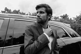 stylish beard man in suit standing near black car