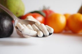 pills in a spoon against a background of vegetables and fruits