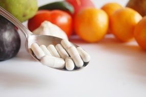 Spoon with pills in the background of vegetables and fruits