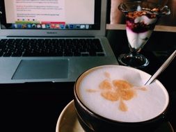 a cup of coffee stands on a table near a laptop