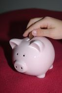 human hand throws a coin into a piggy bank