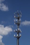 High cell tower on blue sky background with white clouds