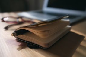 note book with a background of a laptop and glasses