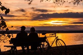 people sit on a bench near lake constance at sunset