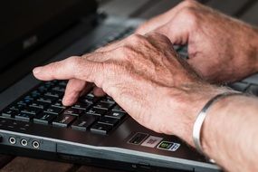 old hands typing on laptop