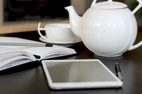 Tea pot,ipad,pen,cup and notepad on the table