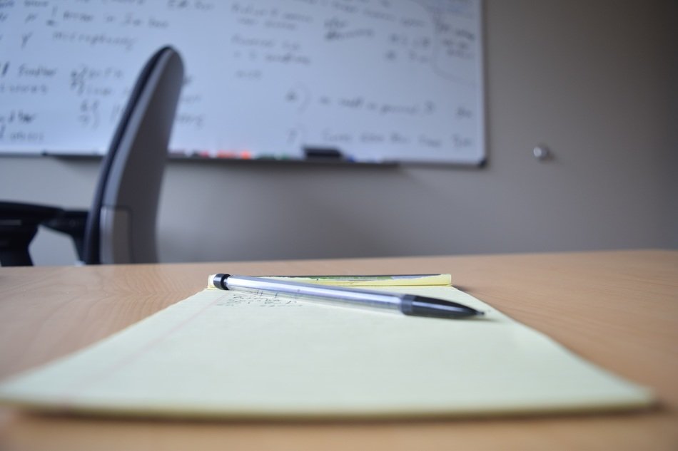 Pen and paper on desk and whiteboard on the background