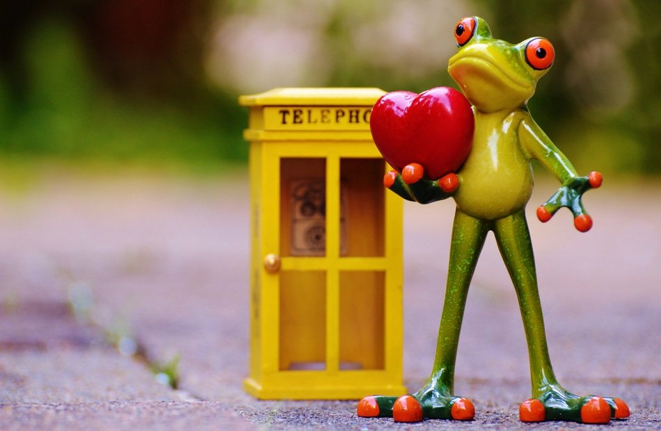 small statue of a green frog holding a heart and standing next to a telephone booth