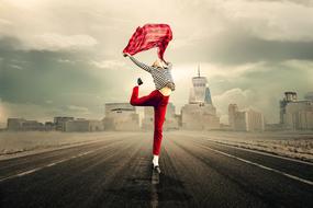 Girl with red scarf jumps on the road with cityscape on background