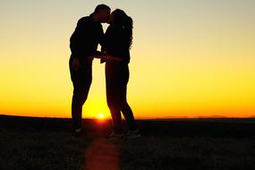 Silhouettes of the couple, kissing, on the beautiful landscape, at colorful and beautiful sunset