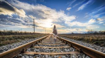 Girl walking away on railway at sunset