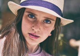 Portrait of a girl with freckles and in hat with violet ribbon