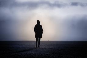 dark silhouette of a girl in autumn clothes against the evening sky
