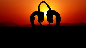 silhouettes of two girls in a yoga pose at sunset