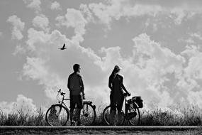 black and white photo of a couple with bicycles on a background of cloudy sky