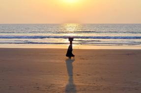 a woman walks along the beach near the sea in India