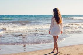 a girl in a white dress walks along the beach in the Canary Islands