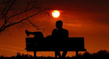 silhouettes of a couple on a bench against a background of orange sunset