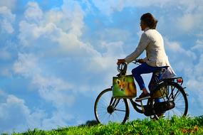 Woman riding bicycle on meadow at sky