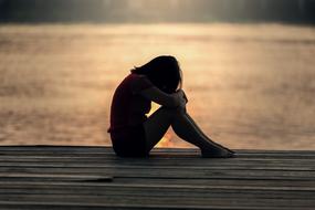 sad girl sitting on the pier in the evening