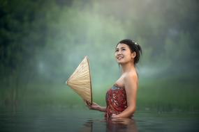 Young Asian woman with traditional hat in hand stands in water