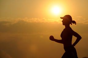 Silhouette of a running woman at beautiful and colorful sunset in clouds
