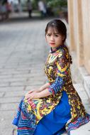 Asian woman, in the colorful, patterned dress, sitting on the street