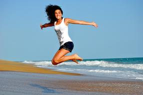 Smiling, jumping woman, on the sandy beach, in light, near the water, with the waves