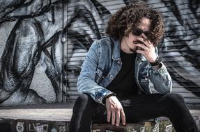 depressed young curly man sits at grunge wall