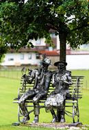 old man and woman sit on bench, metal Sculpture in park